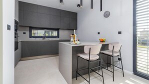 A modern kitchen with dark cabinets, a window, and a dining area with two chairs. - Luxurious home in Vodnjan (Vodnjan)