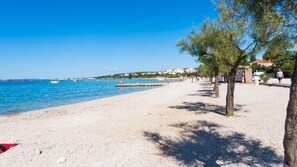 A beach with a pebble shore, a few boats in the water, and a row of trees along the side. - Holiday apartment mit Terrasse (Biograd na Moru)