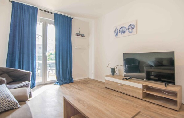 A living room with a wooden coffee table, a sofa, a TV on a wooden stand, and a sliding glass door with blue curtains. - Holiday apartment mit Terrasse (Biograd na Moru)