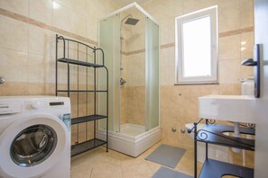 A compact bathroom with a washing machine, a glass-enclosed shower, and a toilet with a shelf. - Holiday apartment mit Terrasse (Biograd na Moru)
