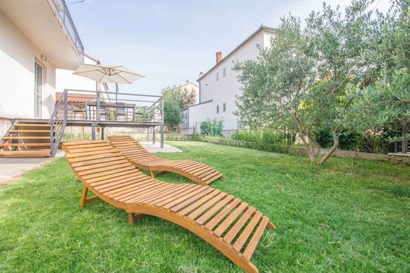 A backyard with two wooden lounge chairs, a staircase, and a white building. - Holiday apartment mit Terrasse (Biograd na Moru)
