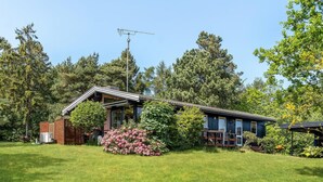 A modern house with a sloped roof, surrounded by a well-maintained lawn and various trees. - Nice home in Fårevejle with WiFi (Fårevejle)
