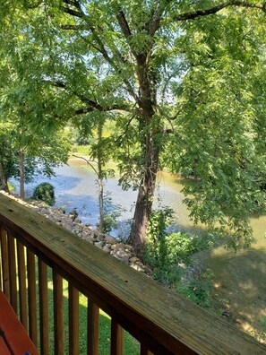 Eine Holzterrasse mit Blick auf einen Fluss, Bäume und eine Rasenfläche.
