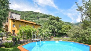 Una piscina con cubierta de madera, rodeada de exuberante vegetación y un edificio amarillo con paredes de piedra.