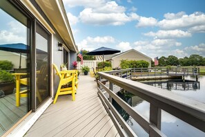Eine Holzterrasse mit gelben Stühlen und einem Tisch, mit Blick auf ein Gewässer und einen Golfplatz.