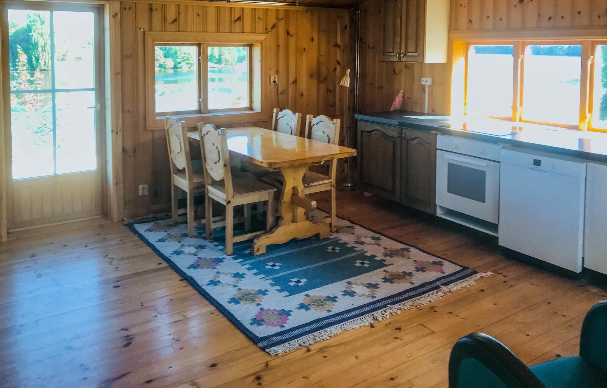 Un intérieur en bois comprenant une table et des chaises, un coin cuisine et de grandes fenêtres.