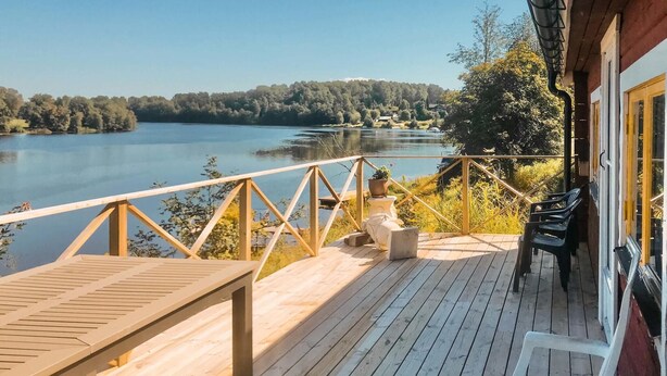 Een houten terras met een tafel en stoelen, met uitzicht op een meer met een bosrijk eiland in de verte.