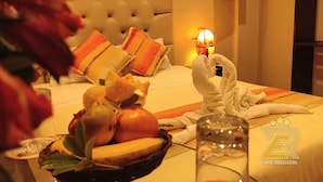 Habitación de hotel con un cabecero capitonado, una lámpara de noche, un frutero y un perchero con toallas.