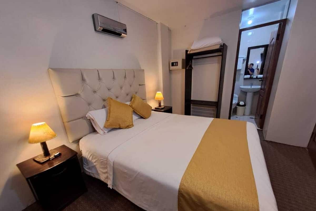 A hotel room with a large bed, two bedside lamps, a headboard, and a mirror above the bed.