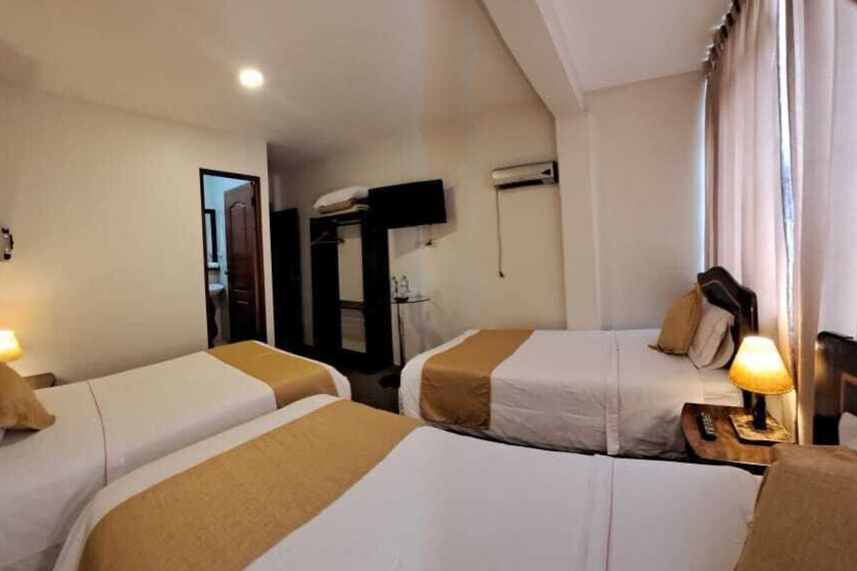 A hotel room with two beds, a nightstand with a lamp, a mirror, and an air conditioning unit on the wall.
