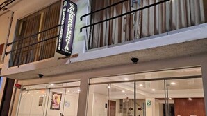 Un hotel con fachada de vidrio, un comedor visible con mesas y sillas, y un letrero sobre la entrada.