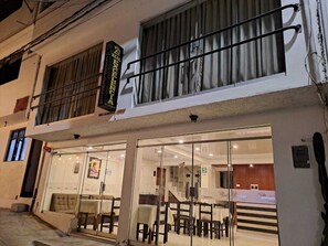 A hotel with a glass facade, a balcony with a metal railing, and a sign above the entrance. - Real Excelencia (Machu Picchu)