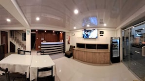 Un vestíbulo de hotel con una recepción, zona de estar y una pantalla de televisión.