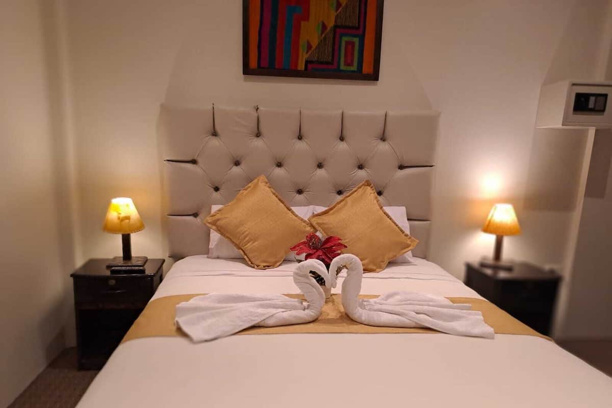 A hotel room with a large bed, two nightstands, and a colorful abstract painting on the wall.
