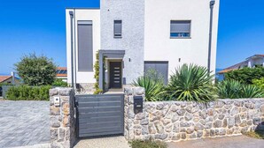A modern two-story house with a stone wall entrance, a gated driveway, and a clear blue sky. - Holiday apartment with pool and air conditioning (Njivice)