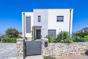 A modern two-story house with a stone wall entrance, a gated driveway, and a clear blue sky.