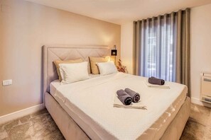 A hotel room with a large bed, a bedside lamp, a window with curtains, and a wall-mounted air conditioner.