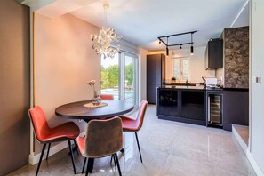 A modern kitchen with a built-in oven, a dining area with a round table and chairs, and a large window providing a view of the outdoors.