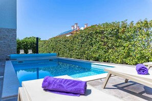 Une piscine avec des chaises longues, un mur en pierre et une haie.