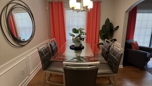 A dining room with a glass-top table, six chairs, a chandelier, and a large plant.