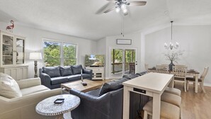 A spacious living room with a gray sectional sofa, a round coffee table, and a dining area with a white table and wooden chairs. - Hideaway Hill - Lakefront Relaxation with Great Amenities (Denver)