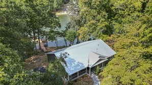 A house with a metal roof, surrounded by dense trees and a lake. - Hideaway Hill - Lakefront Relaxation with Great Amenities (Denver)