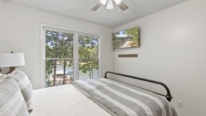 A bedroom with a bed, a ceiling fan, a window with a view of trees and a house, and a framed picture on the wall. - Hideaway Hill - Lakefront Relaxation with Great Amenities (Denver)