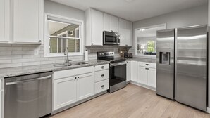 A modern kitchen with white cabinets, stainless steel appliances, and a large window. - Hideaway Hill - Lakefront Relaxation with Great Amenities (Denver)