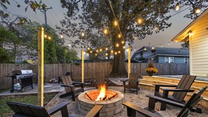 An outdoor patio with a fire pit, seating, and string lights.