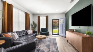 A modern living room with a black leather sofa, a wooden coffee table, and a television mounted on the wall.