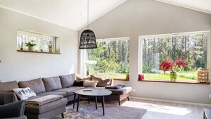 A modern living room with a sectional sofa, a round coffee table, and large windows offering a forest view. - 3 bedroom cozy home in Gotlands Tofta (Gotlands Tofta)