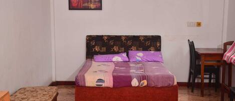 A bedroom with a bed, a chair, a table, and a painting on the wall.