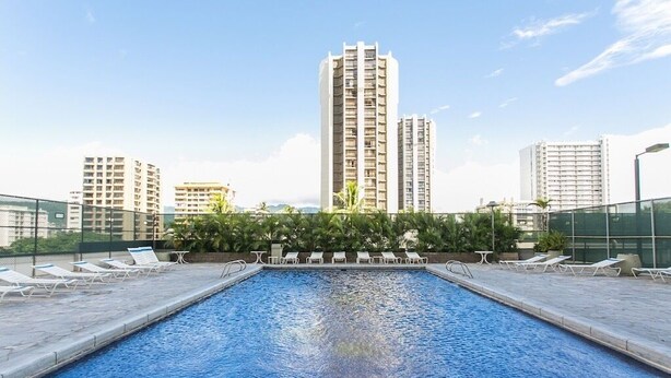 A rooftop swimming pool with lounge chairs and a view of high-rise buildings.