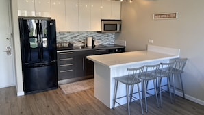 A modern kitchen with a black refrigerator, a microwave, and a white island with bar stools.