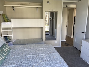 Un dormitorio con literas, un armario, un espejo y una puerta que da a otra habitación.