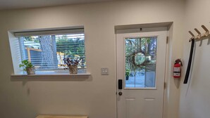 Ein Zimmer mit einer weißen Tür, einem Fenster mit Jalousien, einer kleinen Holzbank, einem blauen Aufbewahrungsbehälter und einem an der Wand montierten Feuerlöscher.