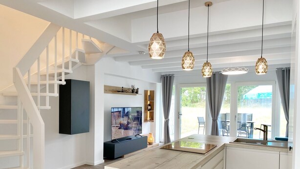 A modern kitchen with a central island, pendant lights, a built-in TV, and a staircase.