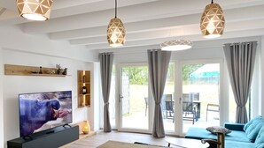 A modern living room with a flat-screen TV, wooden furniture, and pendant lights.