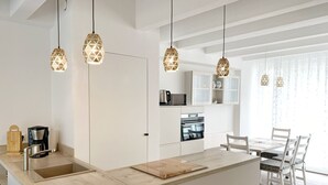 A modern kitchen with a central island, pendant lights, and a dining area with chairs.