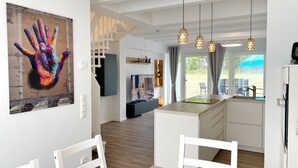 A modern kitchen with a central island, pendant lights, and a dining area with white chairs.