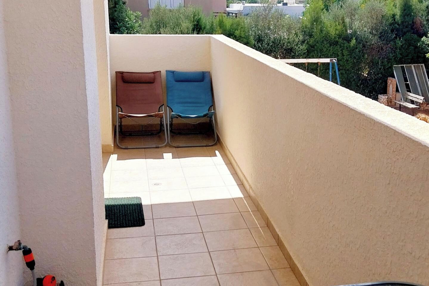 Ein Balkon mit zwei Stühlen, gefliestem Boden und Blick auf Grünflächen und Gebäude.