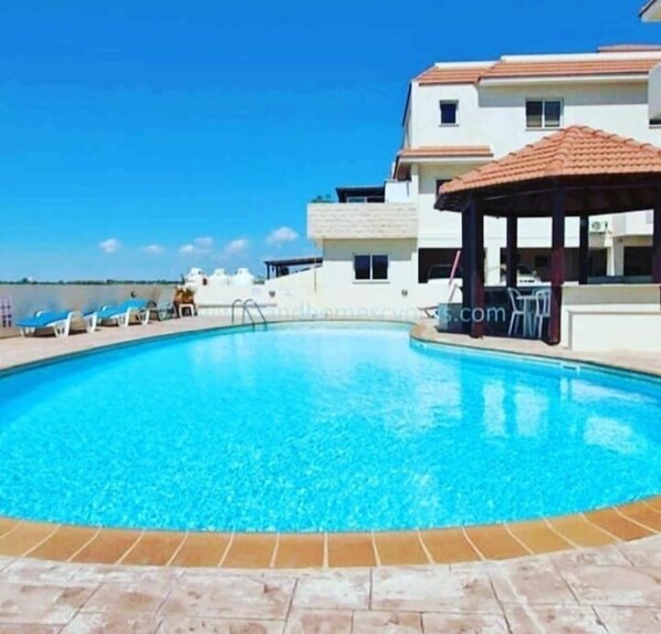 A swimming pool with lounge chairs and a gazebo, surrounded by a building with a tiled roof.