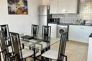 Ett modernt kök med ett matbord i glas, stolar, en mikrovågsugn, en tvättmaskin och skåp.