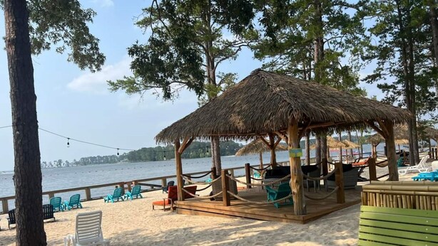 Zona de playa con una estructura de techo de paja, terraza de madera y sillas de playa.