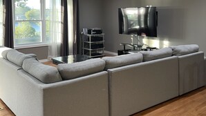 Un salon moderne avec un grand canapé d’angle, un téléviseur à écran plat fixé au mur et un plancher en bois.