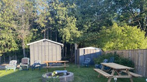 Un jardin avec un abri en bois, un foyer, des tables de pique-nique et des sièges d’extérieur.