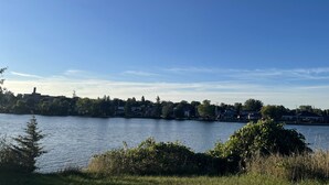 Une vue sur le lac, avec un ciel dégagé, des maisons le long de la rive et un mélange d’arbres et d’arbustes.
