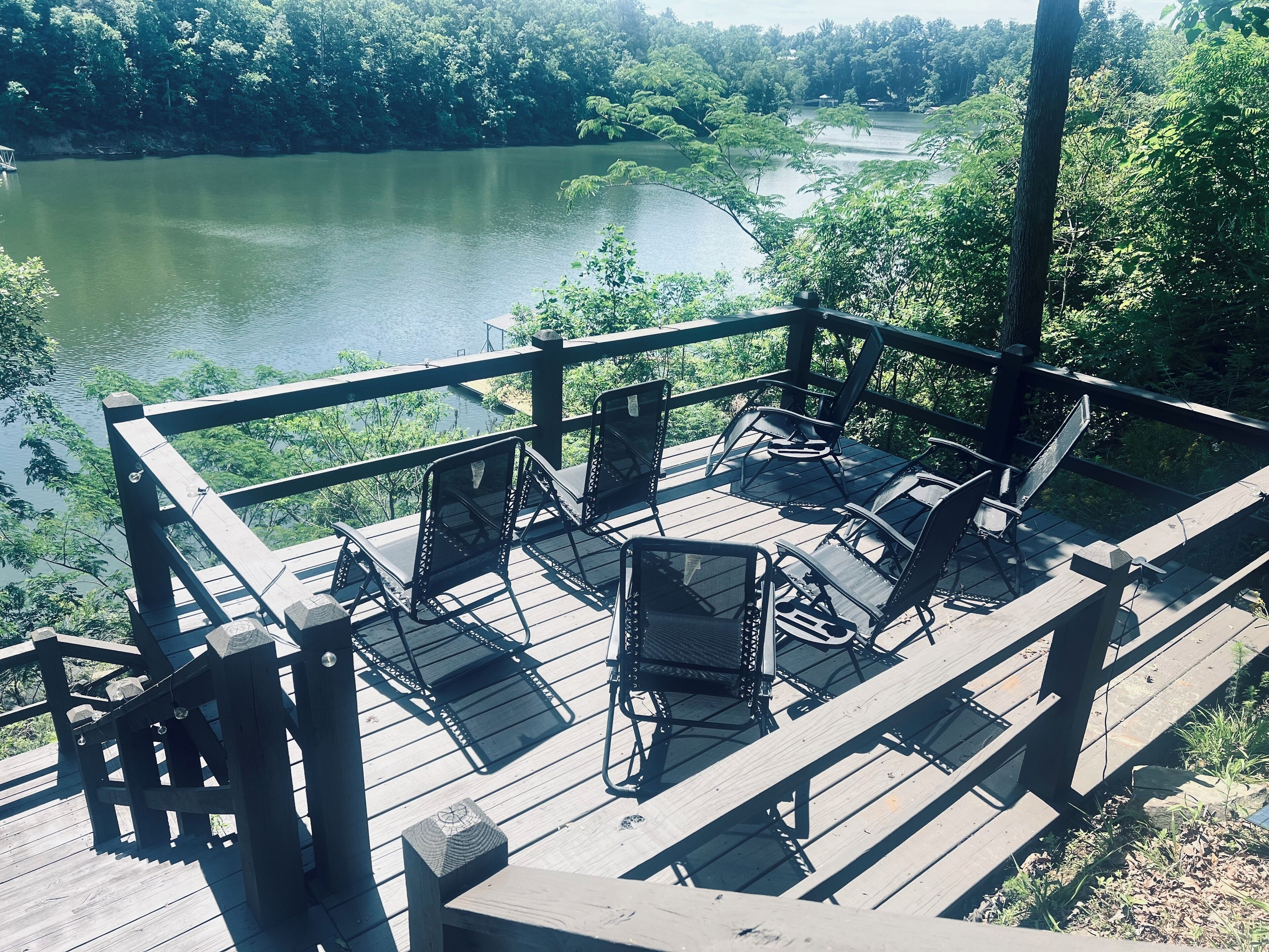 Una terraza de madera con mobiliario exterior y vistas a un lago rodeado de árboles.