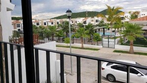 Ein Balkon mit Blick auf eine Wohngegend, darunter Häuser, Palmen und ein Schwimmbad.