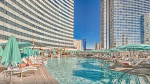 A rooftop pool area with lounge chairs and umbrellas, surrounded by high-rise buildings.